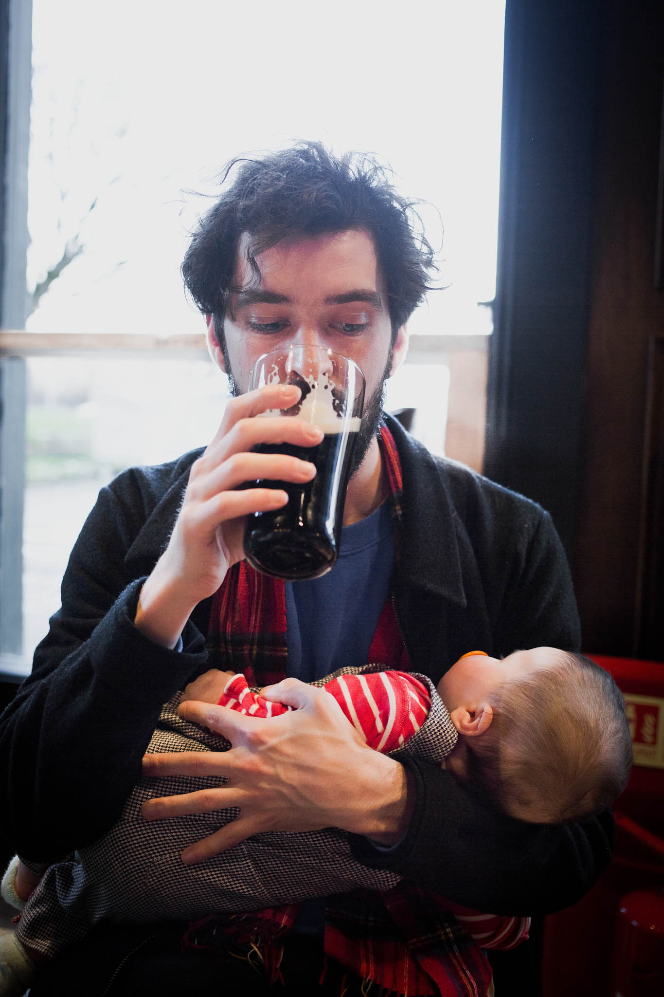 Father drinking pint of guinness watching baby daughter asleep in arms